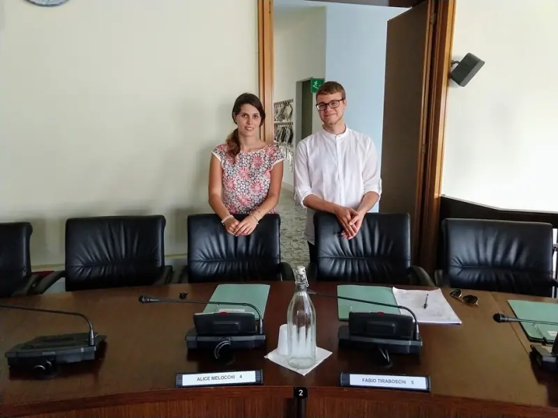 Alice Melocchi e Fabio Tiraboschi in piedi dietro i loro posti in Consiglio Comunale, con le targhette col loro nome sul banco