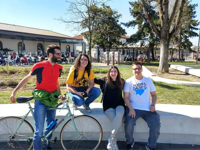 Quattro persone di Nostra Dalmine sedute su un muretto all'aperto in una giornata di sole, una in piedi con la bicicletta
