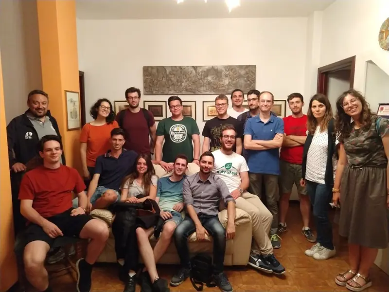 Una ventina di persone di Nostra Dalmine in posa per una foto di gruppo al chiuso, sedute e in piedi attorno a un divano