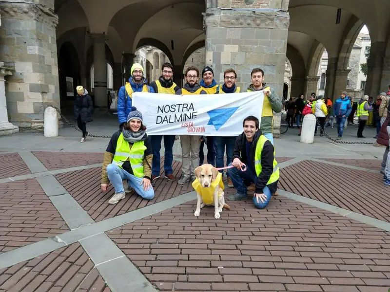 Il gruppo in gilet catarifrangente regge lo striscione «Nostra Dalmine — Lista Giovani» sotto un portico, insieme a un cane